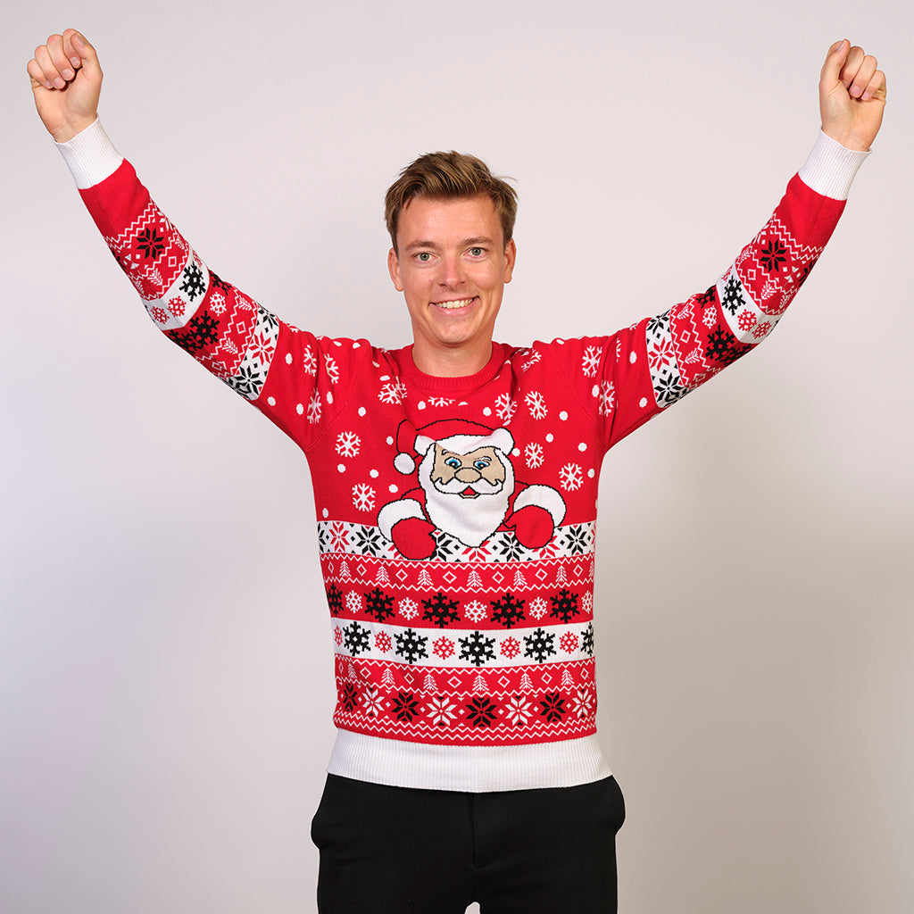 En mand står med armene hævet over hovedet og er iført en rød julesweater.